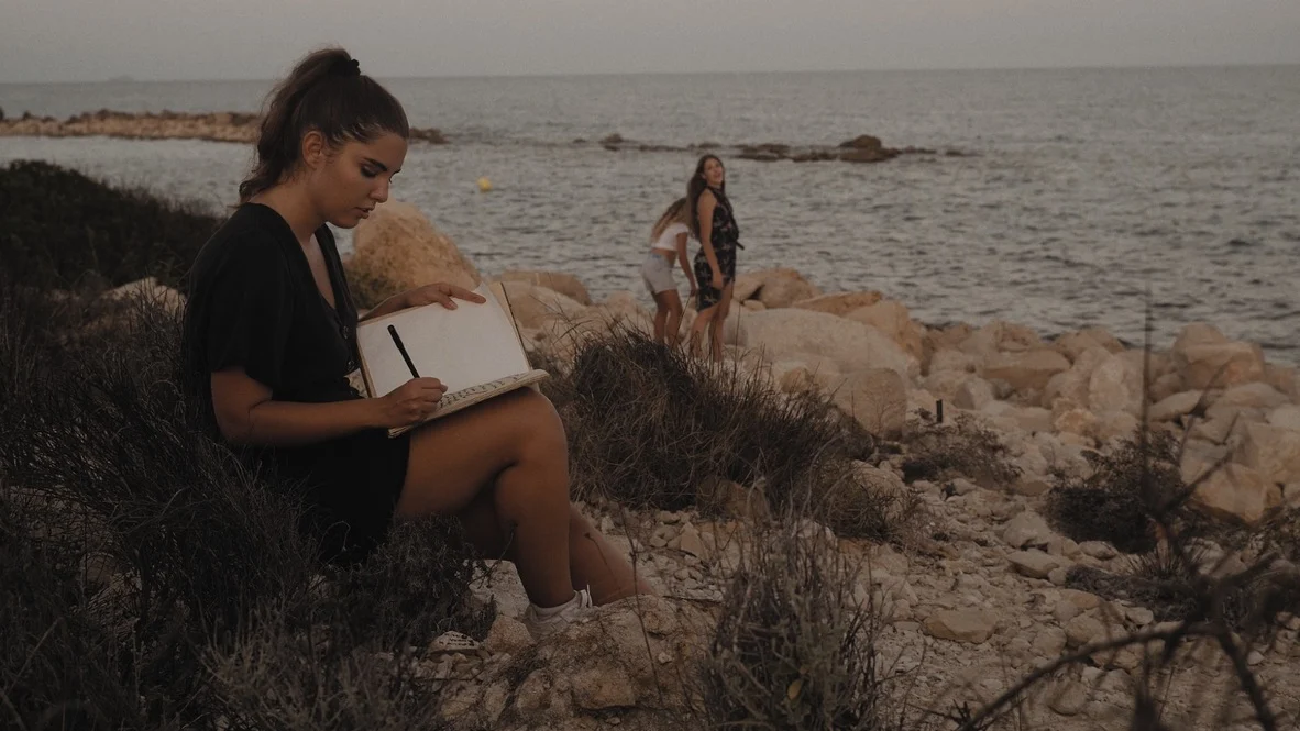 Fotograma de Pandora: una mujer escribe en su cuaderno frente al mar